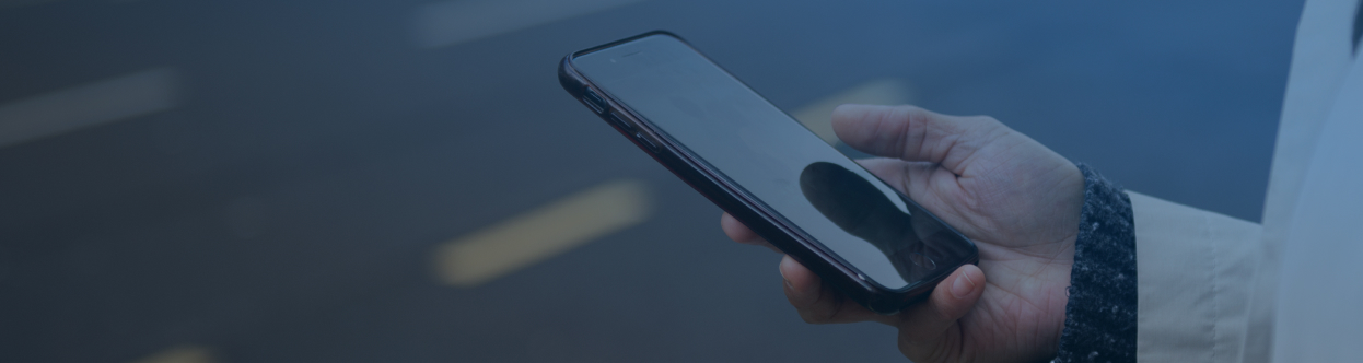 Close-up of a person standing on a roadside and scrolling on a mobile, overlaid with a blue gradient